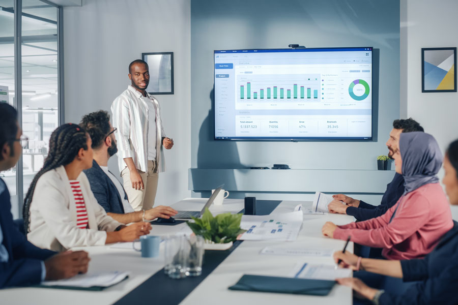 Office Conference Room Meeting Presentation: Black Businessman Talks, Uses Wall TV to Show Fintech Growth with Big Data Analysis, Graphs, Charts, Infographics. Multi-Ethnic e-Commerce Startup Workers
