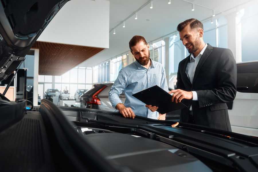 Seller or car salesman and client or customer in car dealership presenting the engine performance of new and used cars in the showroom, the men looking under the hood